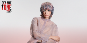 white woman with long blonde hair, which stands in front of a clean grey background looking into the camera